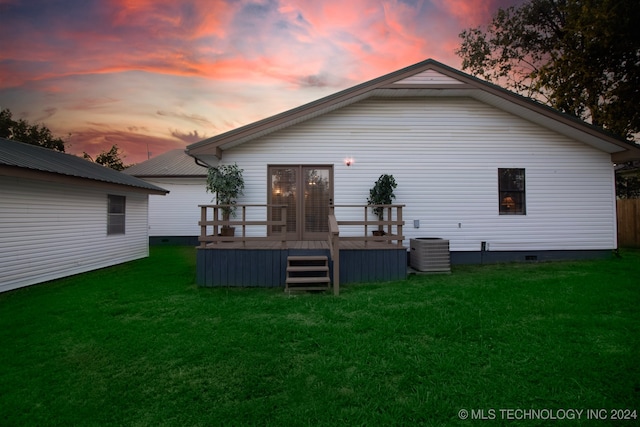 back house at dusk with a yard, a wooden deck, and central AC unit