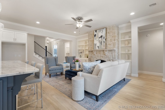 living room featuring a fireplace, built in shelves, light hardwood / wood-style floors, and ceiling fan