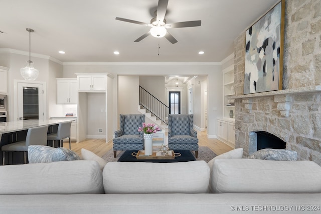 living room featuring light hardwood / wood-style floors, crown molding, a stone fireplace, and ceiling fan