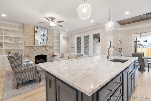 kitchen with sink, a stone fireplace, light hardwood / wood-style flooring, a kitchen island with sink, and ceiling fan