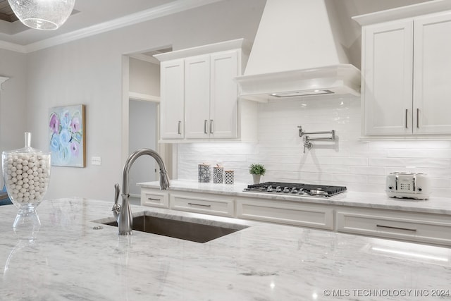 kitchen featuring backsplash, sink, custom range hood, stainless steel gas stovetop, and white cabinets