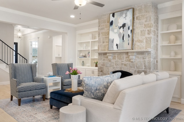 living room featuring ceiling fan, built in shelves, light wood-type flooring, ornamental molding, and a fireplace