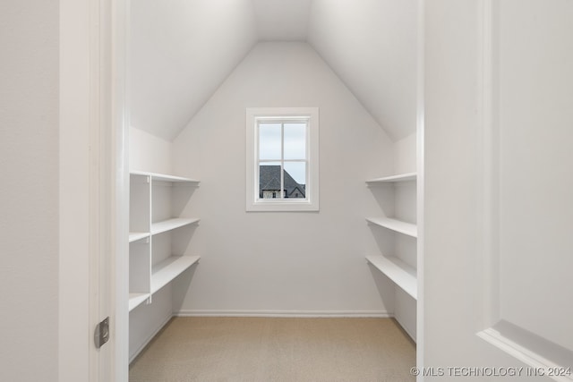 walk in closet with light colored carpet and lofted ceiling