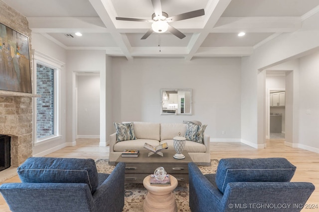 living room featuring ceiling fan, light hardwood / wood-style floors, a stone fireplace, and coffered ceiling