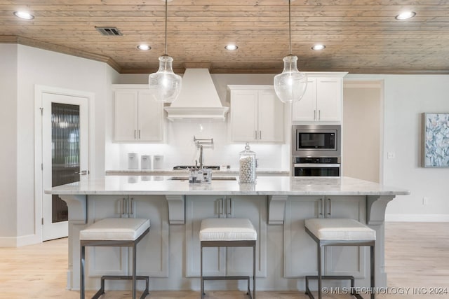 kitchen featuring custom range hood, light wood-type flooring, light stone counters, stainless steel appliances, and white cabinets