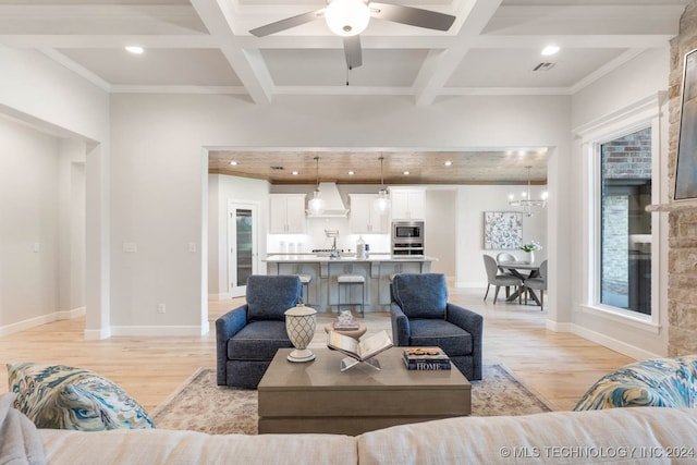 living room with beam ceiling, ceiling fan with notable chandelier, light wood-type flooring, and coffered ceiling