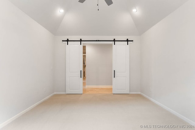 unfurnished room featuring ceiling fan, lofted ceiling, light colored carpet, and a barn door