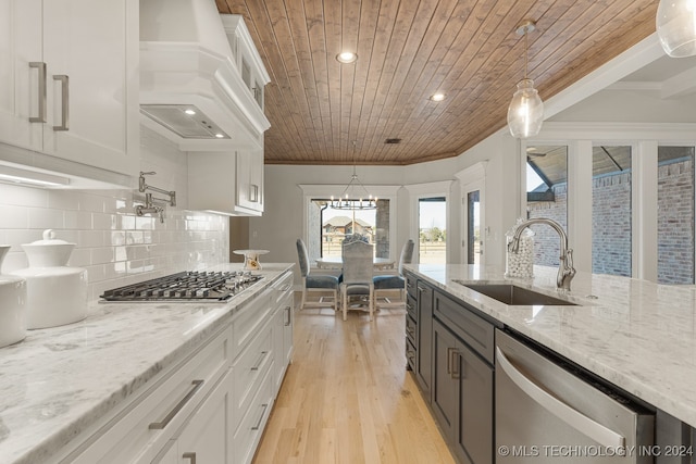 kitchen featuring appliances with stainless steel finishes, premium range hood, light hardwood / wood-style floors, decorative light fixtures, and sink