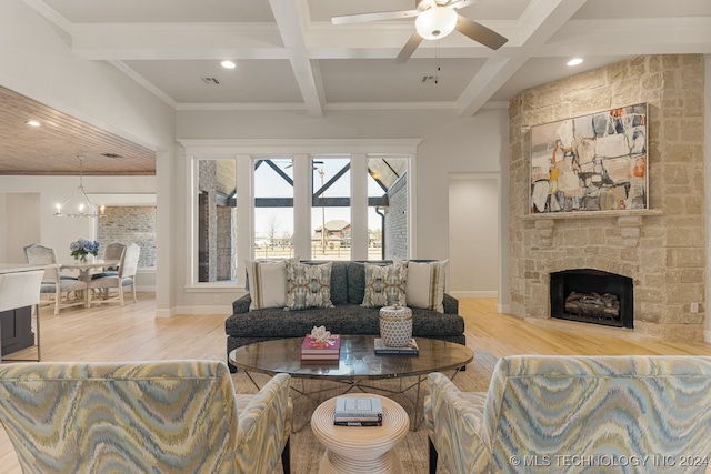 living room with light hardwood / wood-style floors, coffered ceiling, beamed ceiling, ceiling fan with notable chandelier, and a stone fireplace