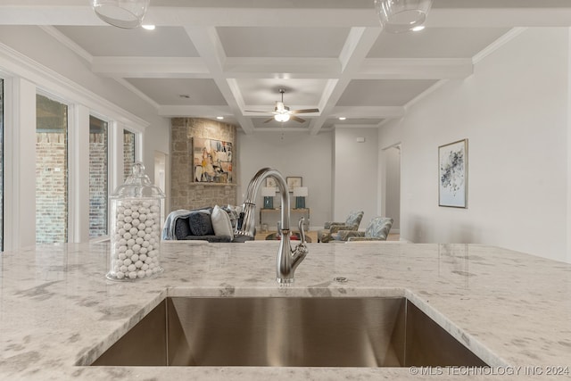 kitchen with sink, beamed ceiling, light stone countertops, coffered ceiling, and ceiling fan