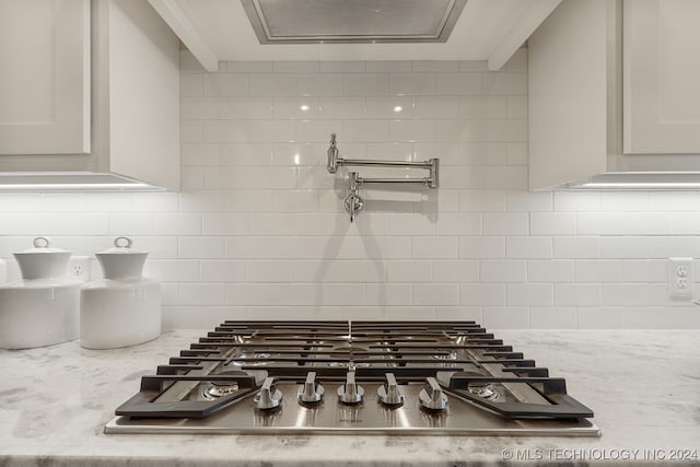 room details with tasteful backsplash, stainless steel gas cooktop, white cabinetry, and light stone counters