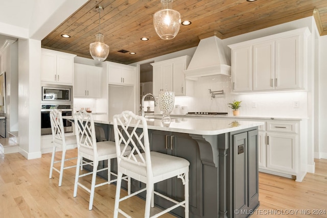 kitchen with appliances with stainless steel finishes, wood ceiling, white cabinets, light hardwood / wood-style flooring, and a center island with sink