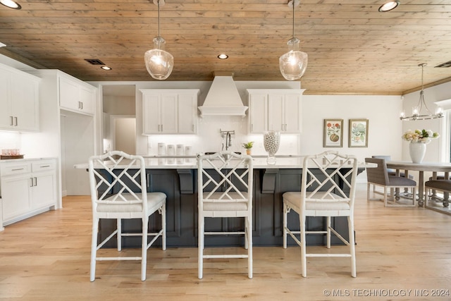 kitchen with hanging light fixtures, white cabinetry, wooden ceiling, custom range hood, and a center island with sink