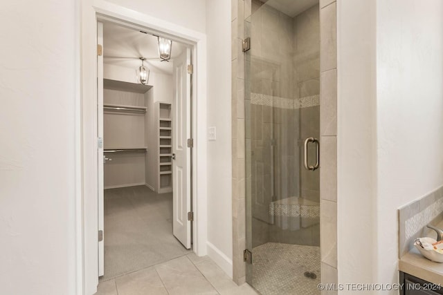 full bathroom with a stall shower, a walk in closet, tile patterned flooring, and baseboards