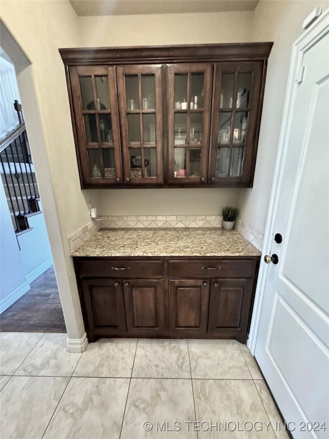 bar featuring light stone countertops, light tile patterned floors, and dark brown cabinetry