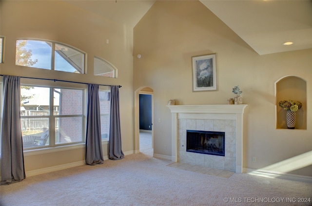 unfurnished living room featuring light carpet, high vaulted ceiling, and a tiled fireplace