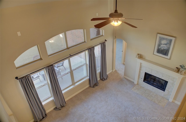 carpeted living room with a tile fireplace, a high ceiling, and ceiling fan