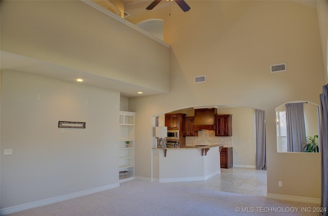 unfurnished living room with ceiling fan, light colored carpet, and a towering ceiling