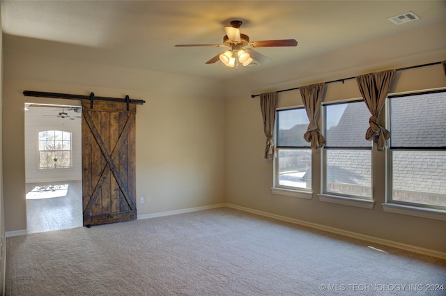 carpeted empty room with plenty of natural light, a barn door, and ceiling fan