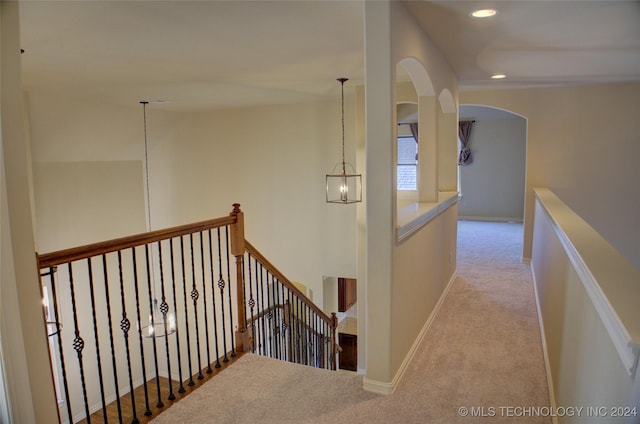 hallway with light carpet and a notable chandelier