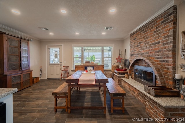 dining space featuring brick wall, ornamental molding, a textured ceiling, and a brick fireplace