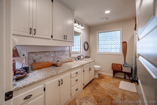 kitchen featuring white cabinetry, ornamental molding, sink, light stone counters, and light tile patterned floors