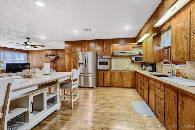 kitchen with light wood finished floors, brown cabinetry, stainless steel appliances, under cabinet range hood, and a sink