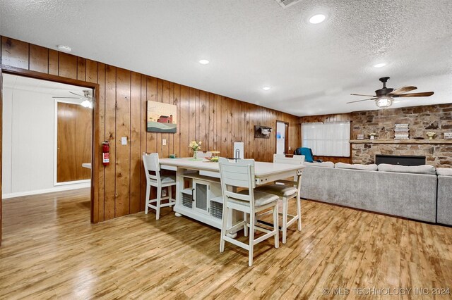 dining room with ceiling fan, a textured ceiling, wood walls, and light hardwood / wood-style floors