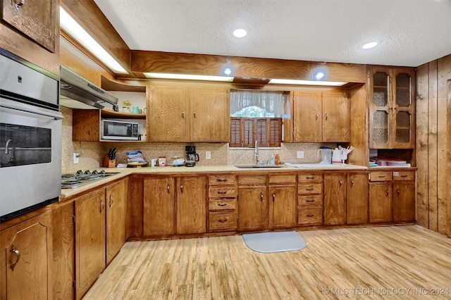 kitchen with light wood-type flooring, appliances with stainless steel finishes, brown cabinets, and a sink