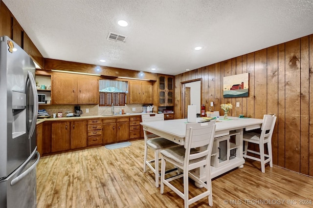 kitchen with light wood finished floors, visible vents, stainless steel fridge with ice dispenser, brown cabinets, and light countertops