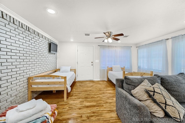 bedroom featuring brick wall, light wood-style flooring, visible vents, and a ceiling fan