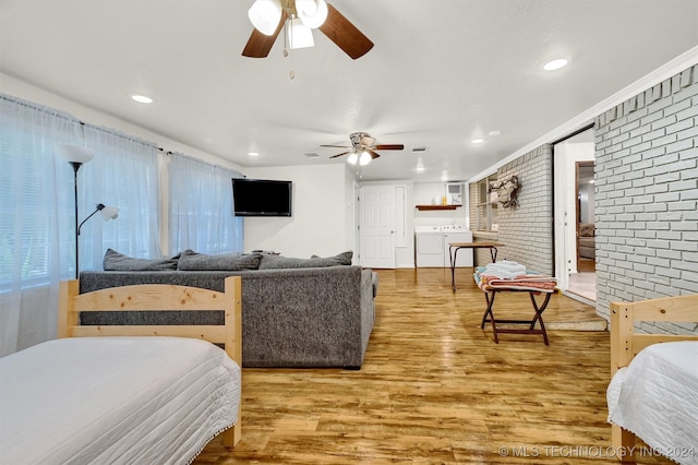 bedroom featuring ceiling fan, light hardwood / wood-style flooring, brick wall, washer and dryer, and connected bathroom