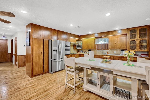 kitchen with light wood finished floors, stainless steel appliances, visible vents, brown cabinetry, and a sink