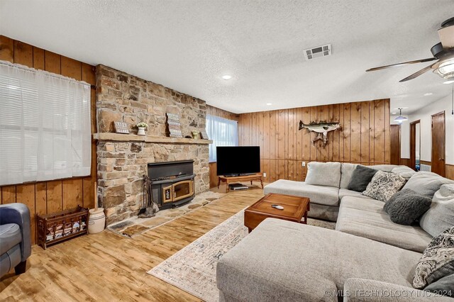 living room with ceiling fan, a stone fireplace, light hardwood / wood-style flooring, and wooden walls