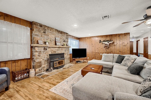 living area with a textured ceiling, wooden walls, wood finished floors, a ceiling fan, and visible vents