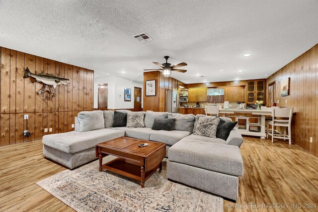 living room with wood walls, ceiling fan, light hardwood / wood-style floors, and a textured ceiling