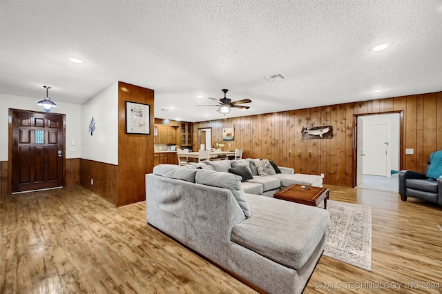 living room featuring a textured ceiling, light hardwood / wood-style flooring, ceiling fan, and wood walls