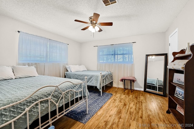 bedroom with a textured ceiling, ceiling fan, and light wood-type flooring