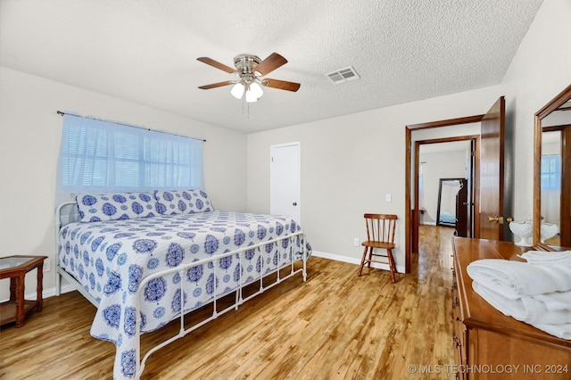 bedroom with ceiling fan, light wood-type flooring, and a textured ceiling