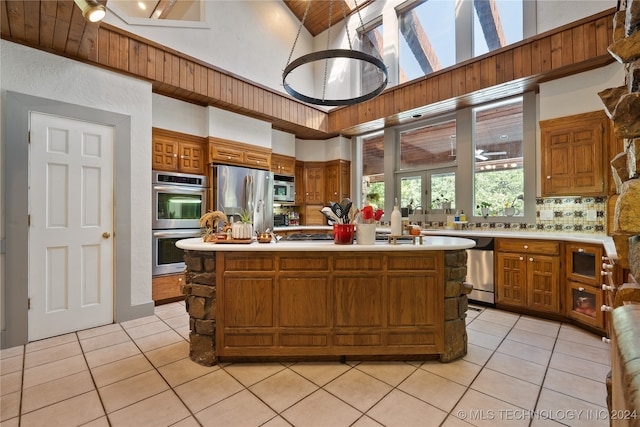 kitchen featuring appliances with stainless steel finishes, light tile patterned flooring, a center island, and tasteful backsplash