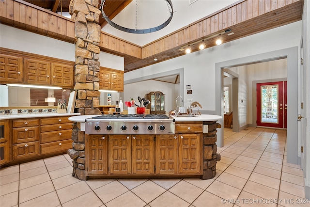 kitchen featuring decorative backsplash, a towering ceiling, beamed ceiling, light tile patterned floors, and stainless steel gas stovetop