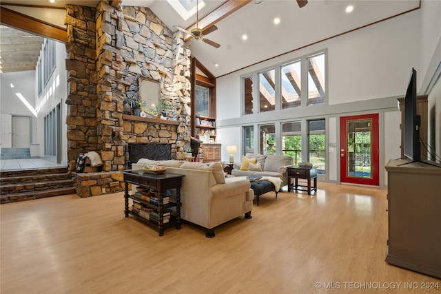 living room featuring high vaulted ceiling, a fireplace, light wood-type flooring, ceiling fan, and a skylight