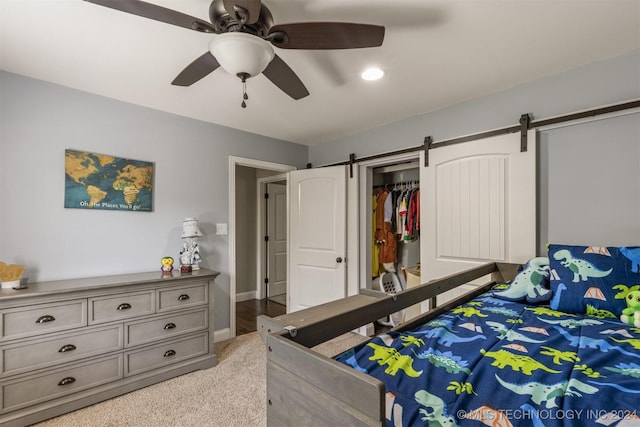 bedroom featuring a barn door, a closet, a ceiling fan, and light colored carpet