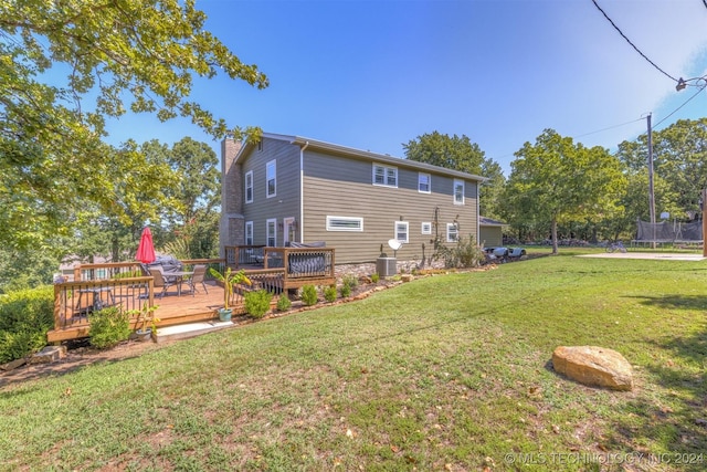 rear view of house with a trampoline, a yard, a chimney, central AC, and a deck