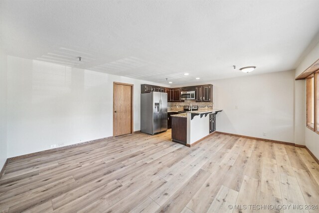 kitchen featuring stainless steel appliances, decorative backsplash, dark brown cabinets, light wood-type flooring, and kitchen peninsula