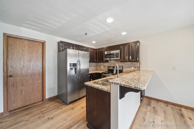 kitchen featuring light wood-type flooring, kitchen peninsula, appliances with stainless steel finishes, and light stone counters