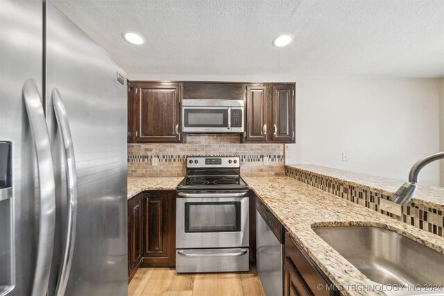 kitchen featuring appliances with stainless steel finishes, light hardwood / wood-style floors, decorative backsplash, sink, and light stone countertops