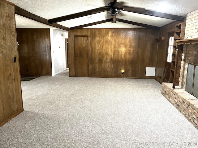 unfurnished living room featuring wood walls, a brick fireplace, a textured ceiling, ceiling fan, and light colored carpet