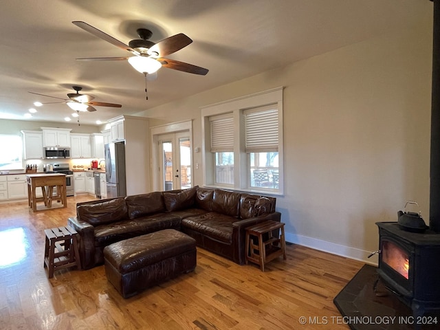 living room featuring a wood stove, ceiling fan, and light hardwood / wood-style floors