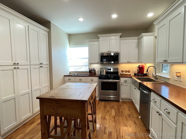 kitchen featuring wood counters, stainless steel appliances, sink, white cabinetry, and light wood-type flooring